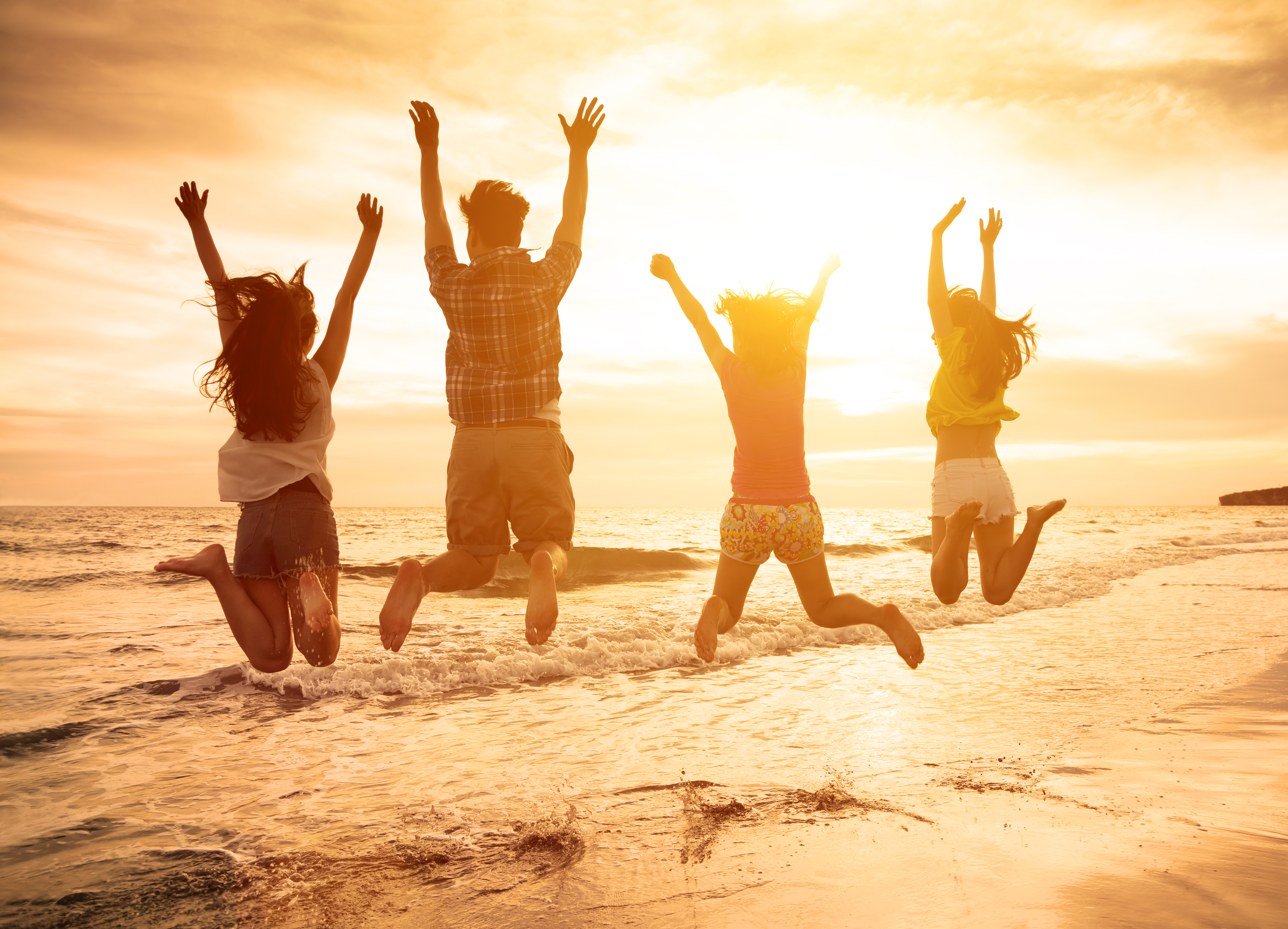 group of happy young people jumping on the beach